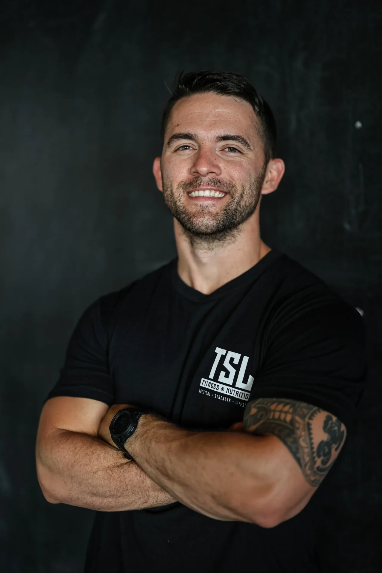 A man with tattoos standing in front of a black wall.