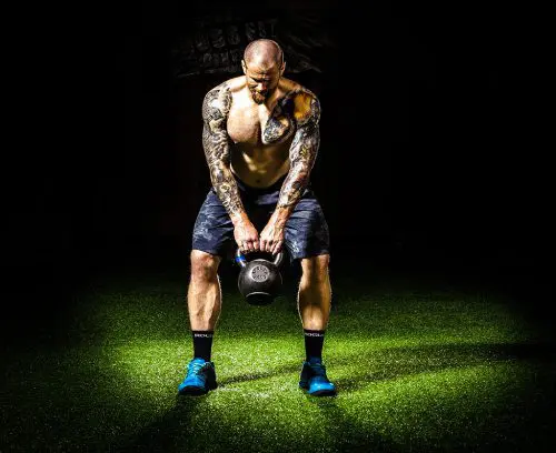 A man with tattoos is holding a kettlebell.